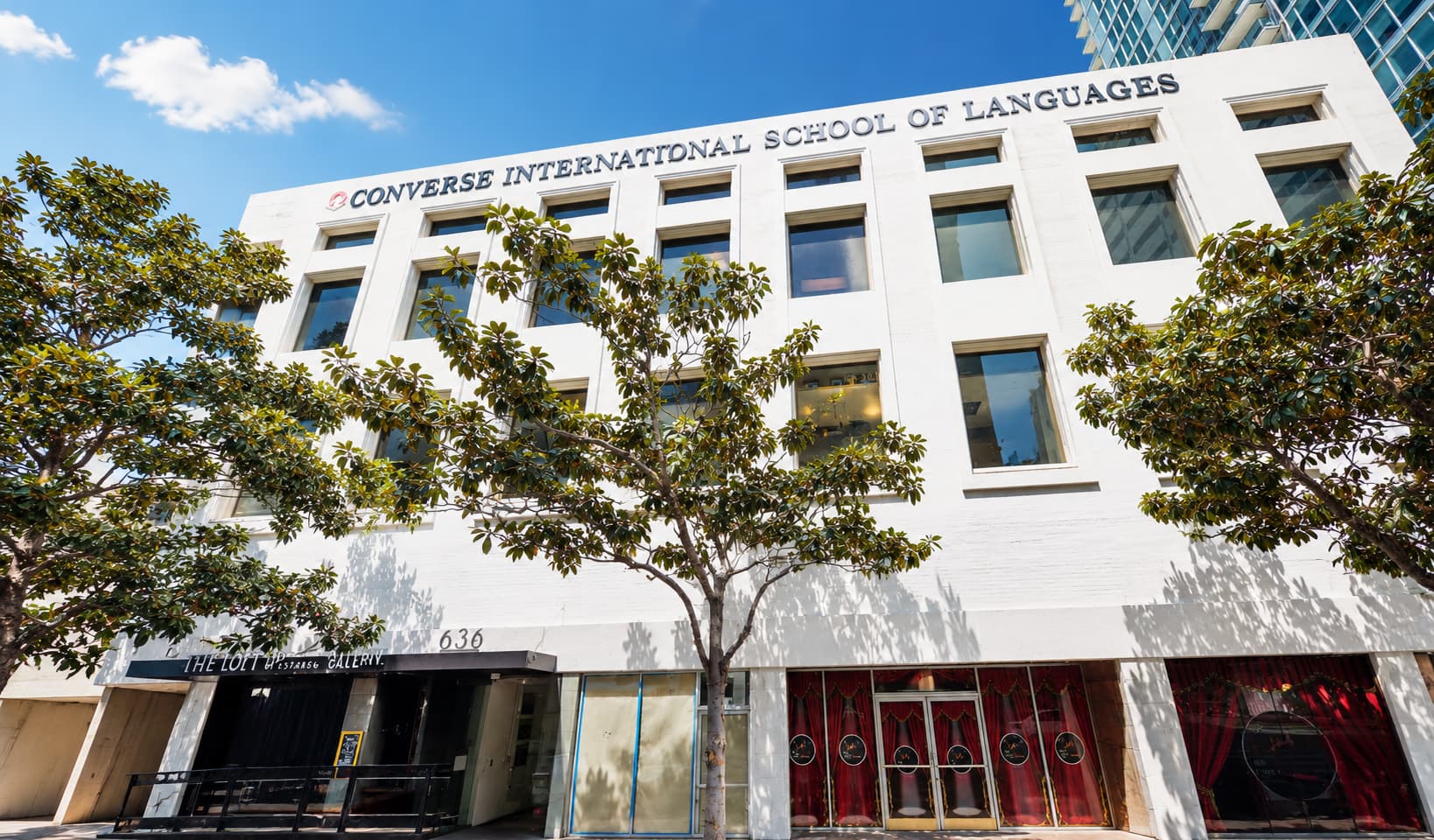 Converse International School of Languages の校舎外観。サンディエゴ中心部のブロードウェイ沿いに位置する白い外壁の建物を、青空と街路樹を背景に見上げるようなアングルで撮影した様子。