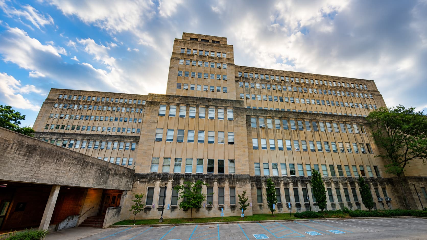 インディアナ大学付属語学学校（Intensive English Program）が開講される歴史ある大学施設を、青空と印象的な雲を背景に16:9のヒーロー画像として表現した外観風景